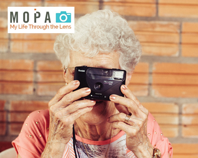 elderly woman holds up a camera to her face