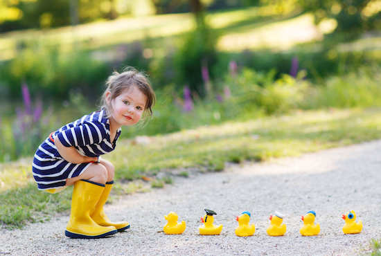 young girl in rain boots with a row of 5 rubber ducks