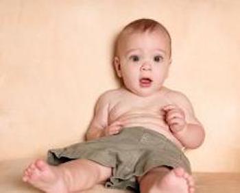 Baby leaning against a wall wearing shorts