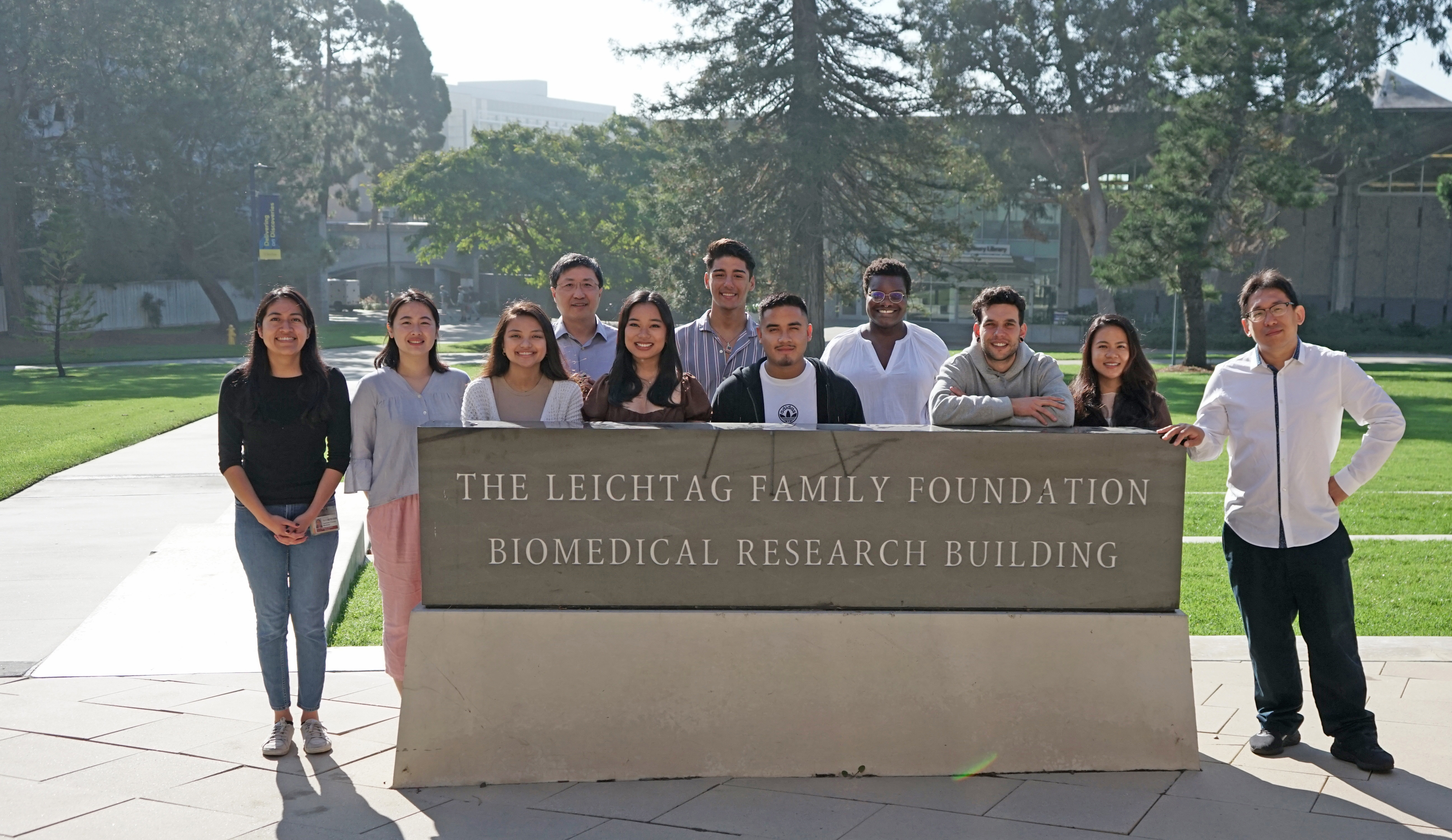 zheng lab members standing outside in front of the leichtag biomedical research building sign